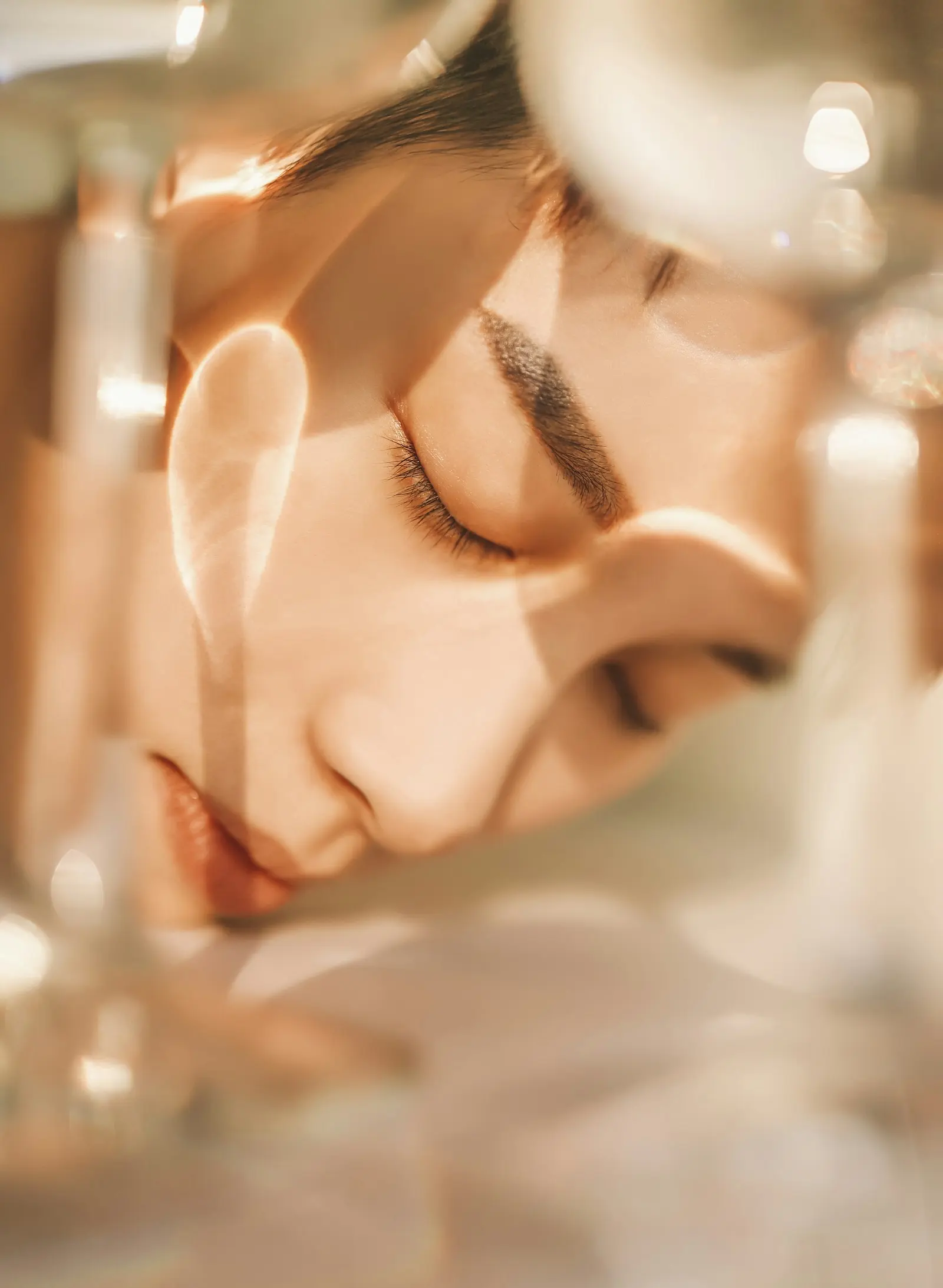Woman with eyes closed, warm light refracted through glass across her face